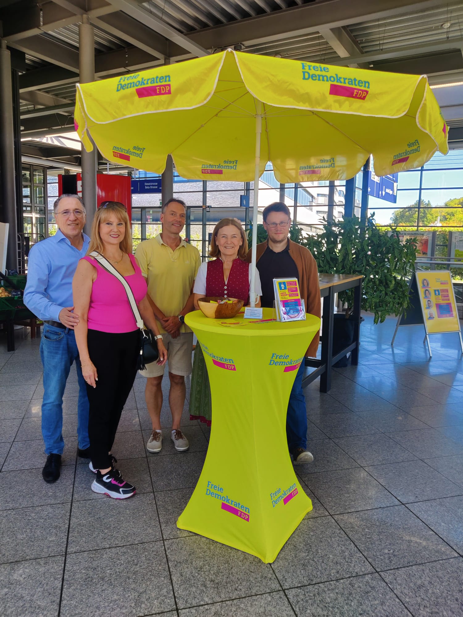 Bürgermeisterkandidatin Anette Westarp steht mit weiteren FDP-Mitgliedern an einem gelben FDP-Stand mit Schirm vor dem Unverpacktladen in Unterföhring.